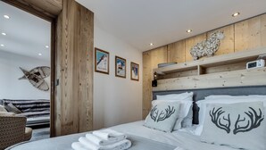 Une chambre à coucher avec une tête de lit en bois, un lit recouvert de draps blancs et agrémenté de coussins décoratifs, une étagère fixée au mur avec un objet décoratif, et un tableau encadré accroché au mur.