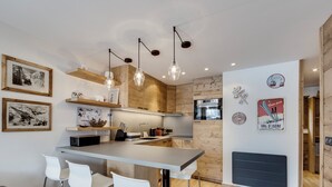 Une cuisine moderne avec des meubles en bois, un îlot central doté de tabourets de bar, des luminaires suspendus et des éléments décoratifs fixés au mur.