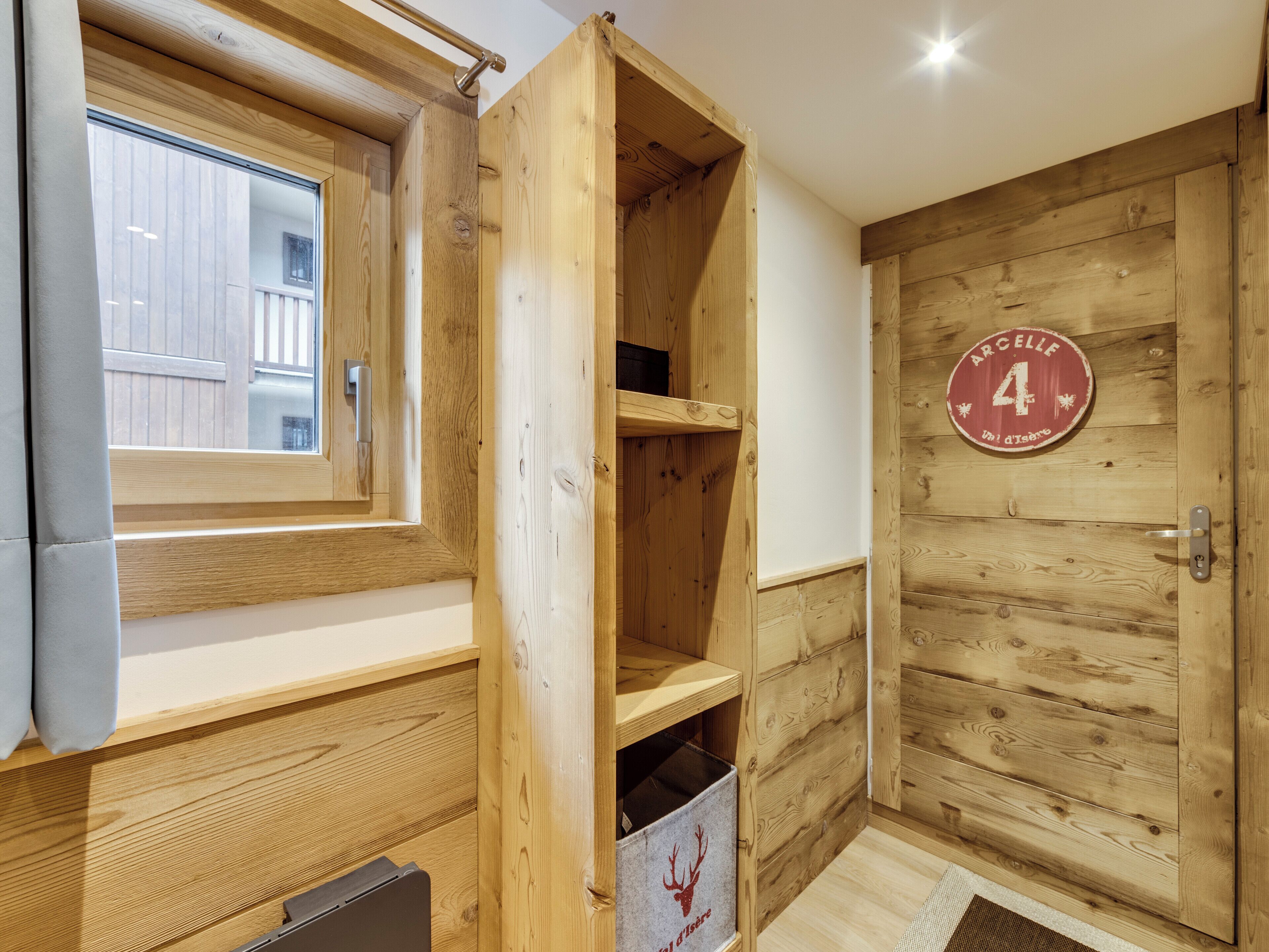 A wooden interior with a window, a door with a number plaque, and a shelf unit.