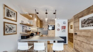 Une cuisine moderne agrémentée d’éléments en bois, dotée d’un îlot central, de tabourets de bar blancs et de différents éléments décoratifs sur les murs.