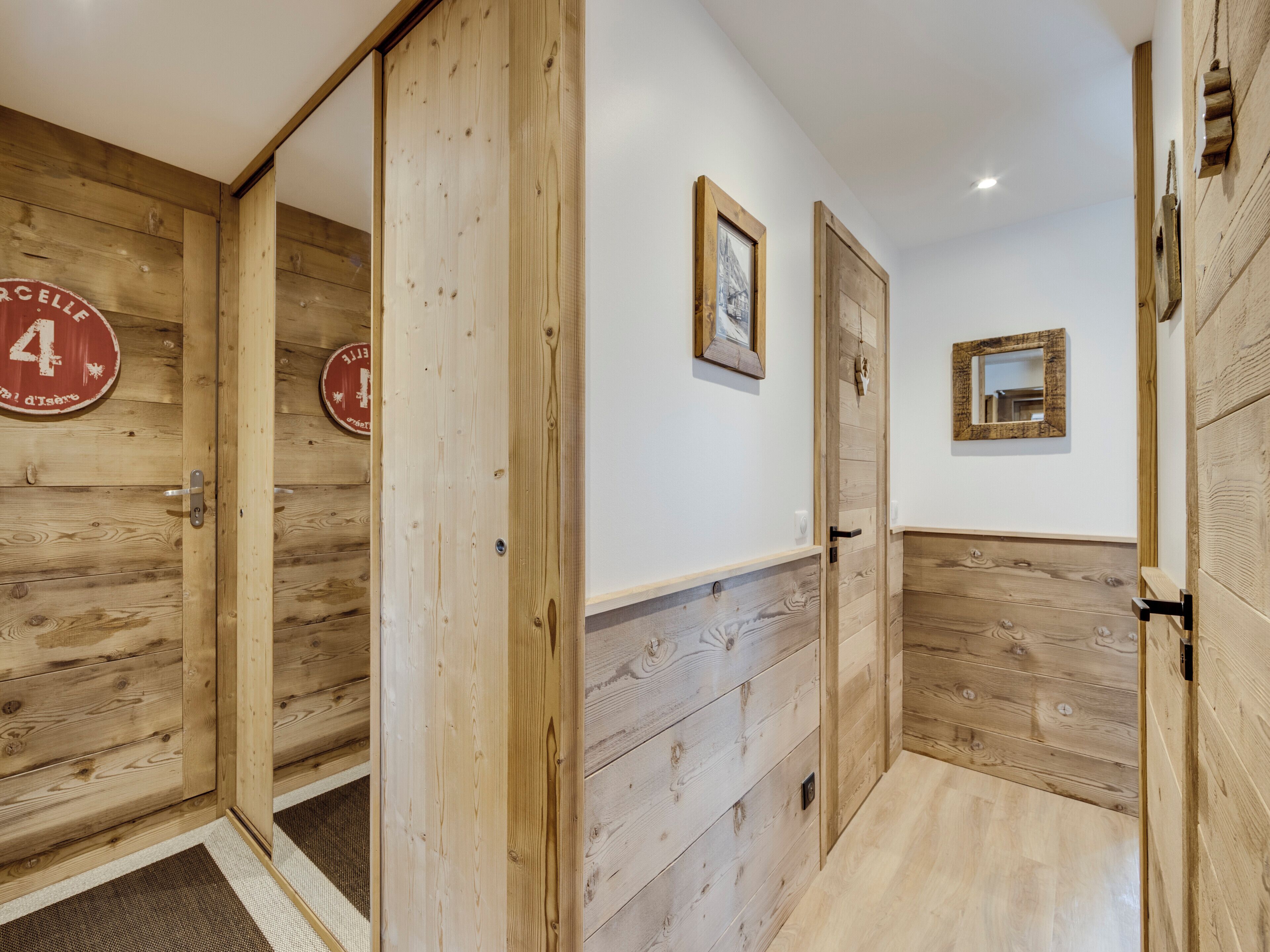 Un couloir aux murs et aux portes en bois, un petit miroir et un tableau encadré accroché au mur.