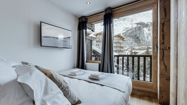Une chambre à coucher moderne avec une grande fenêtre, un lit recouvert de draps blancs et un tableau encadré accroché au mur.