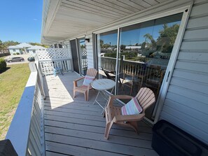 A covered outdoor deck with two chairs and a small table, a white railing, and a view of the surrounding area. - Charming 1-bedroom apartment in amazing Nokomis (Nokomis)