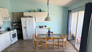 Eine kompakte Küche mit Mikrowelle, Herd und Kühlschrank, ein Essbereich mit Glastisch und Stühlen sowie eine Couch mit Kissen.
