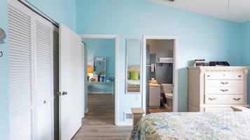 Un dormitorio con cama, cómoda y armario. Hay un pasillo que conduce a un baño.
