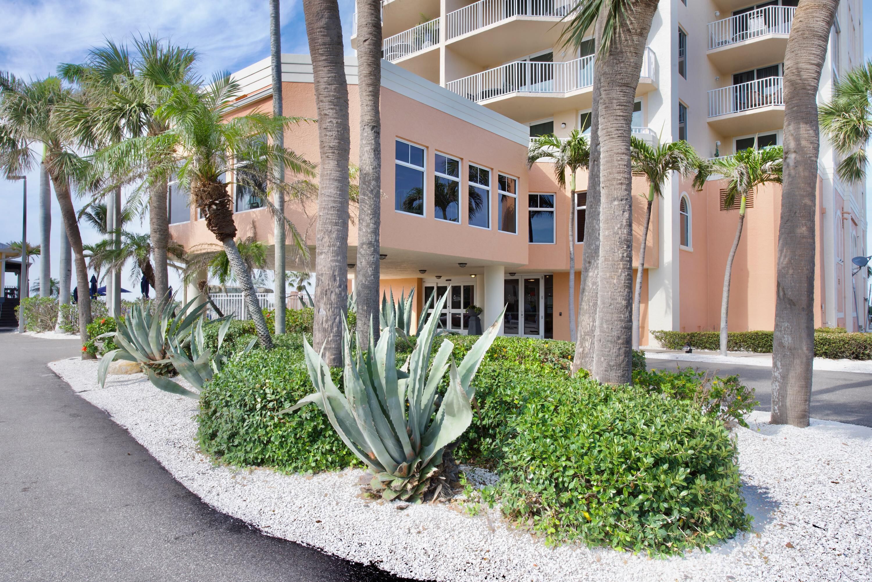 A multi-story hotel with balconies, palm trees, and a well-maintained garden.