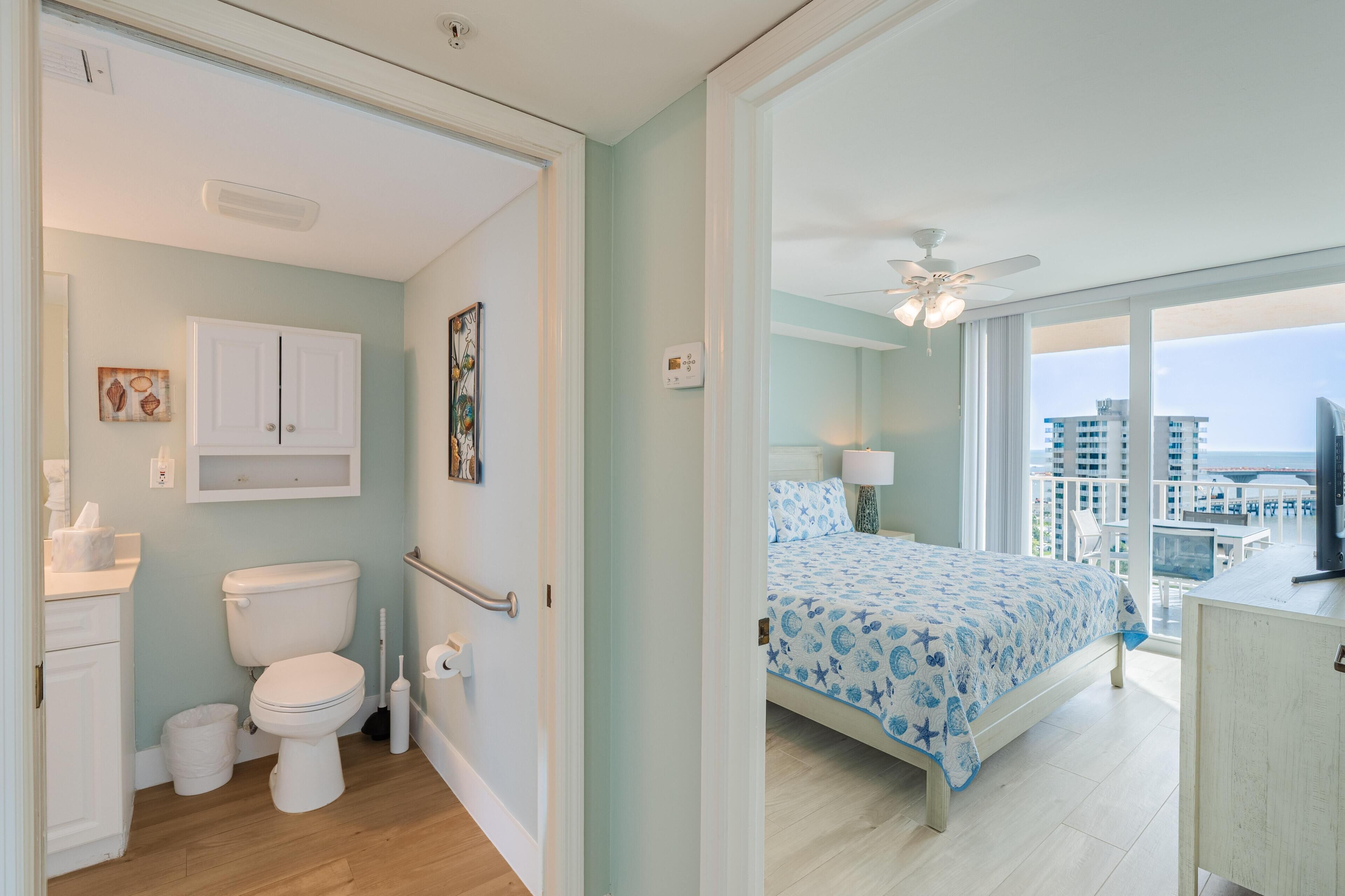 A bedroom with a bed, a balcony with a view, and a bathroom with a toilet and sink.