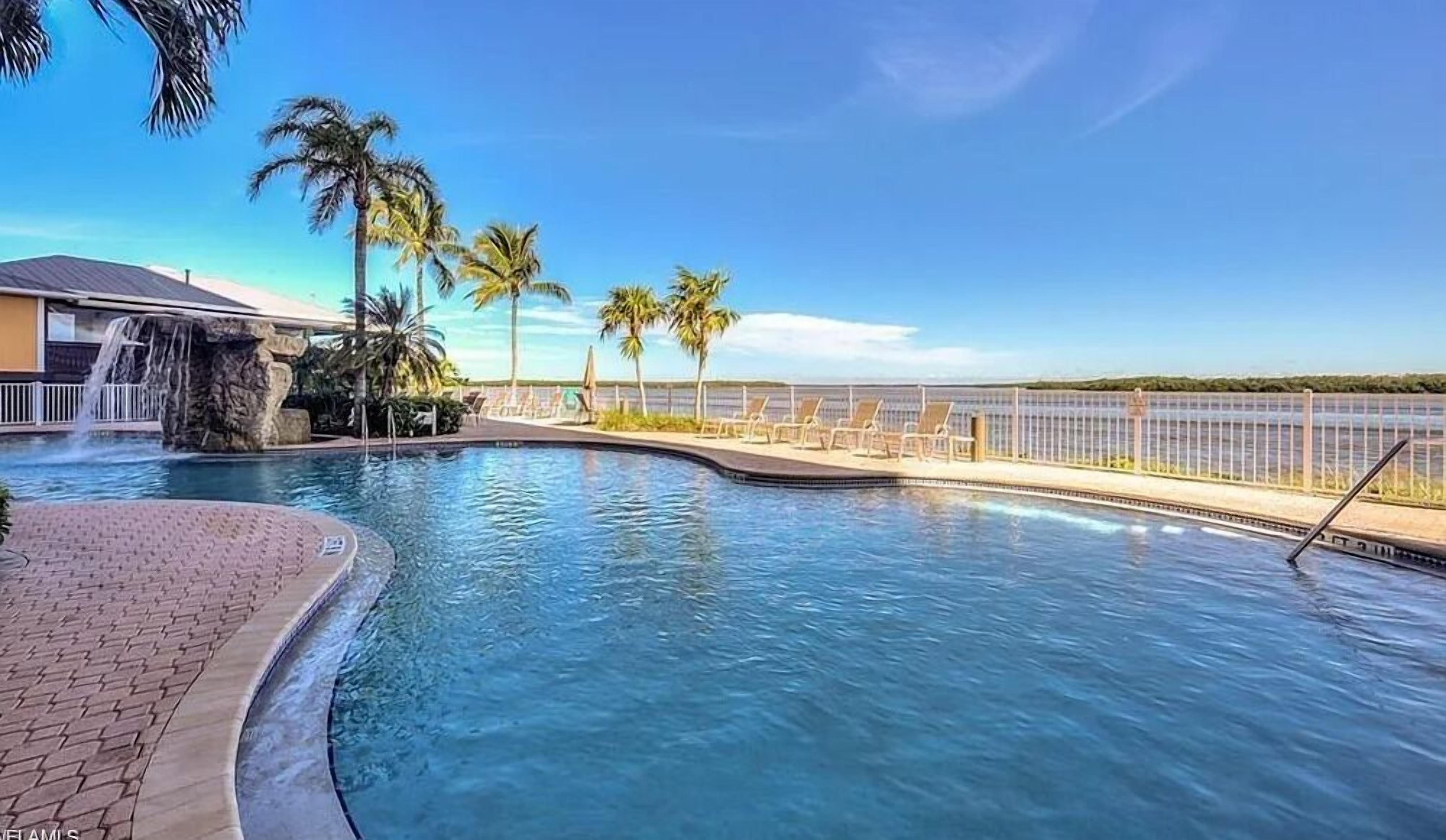 A swimming pool with a waterfall feature, palm trees, and a view of the ocean.