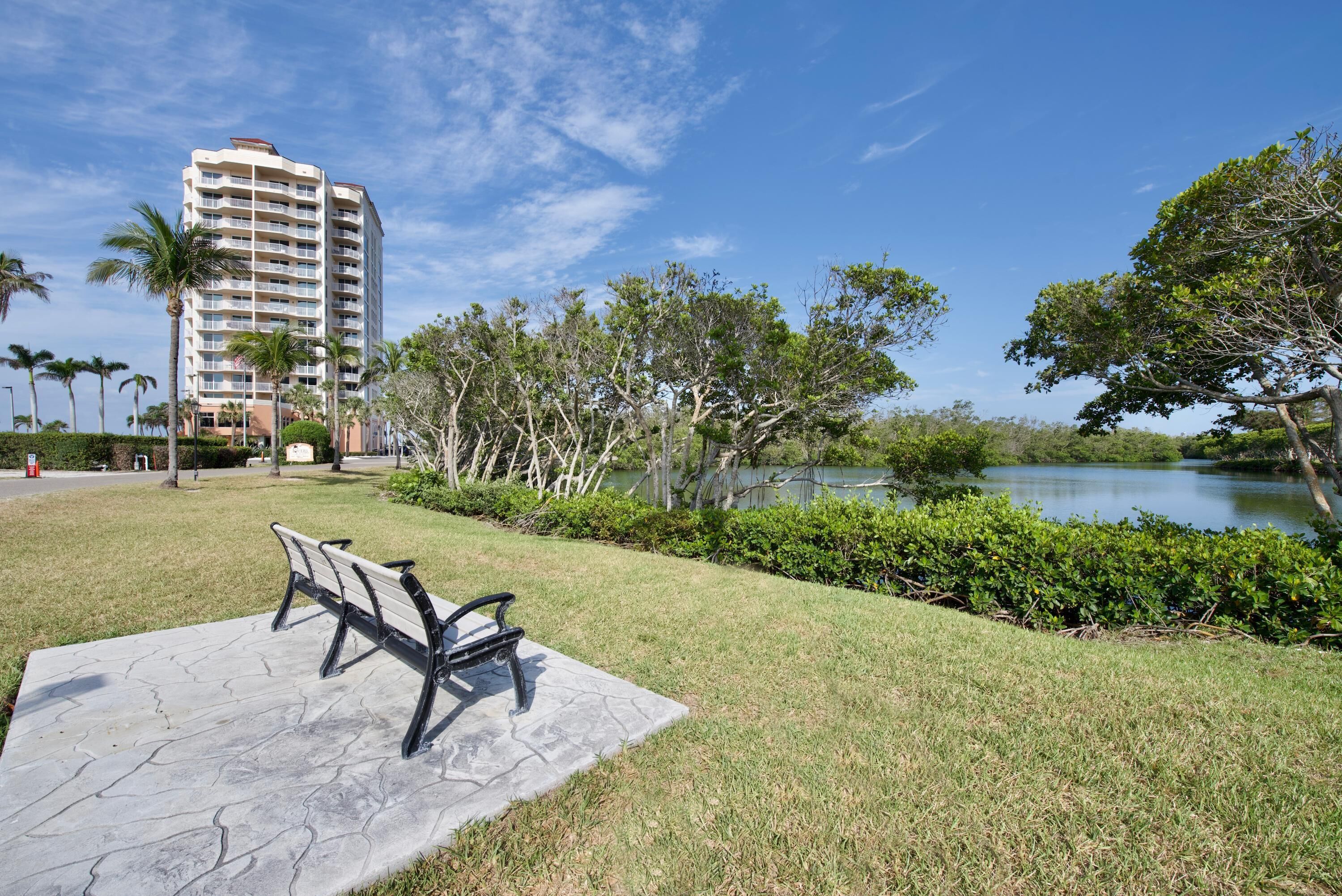 A park with a bench, a lake, and a tall building in the background.