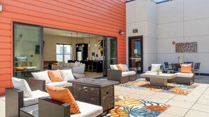 Un espace patio extérieur aménagé avec des meubles en osier, un tapis à motifs et une vue sur l’intérieur grâce à une porte vitrée.