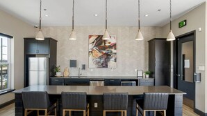 Une cuisine moderne dotée d’un îlot central, de tabourets de bar, de luminaires suspendus et d’un grand tableau abstrait accroché au mur.