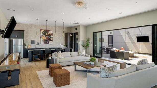 Un salon moderne comprenant un canapé, une table basse et des poufs. Il y a également un coin cuisine avec un réfrigérateur et un coin repas avec une table et des chaises.