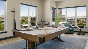 Une table de billard dans une pièce moderne avec de grandes fenêtres, une vue sur la ville et un petit coin salon.