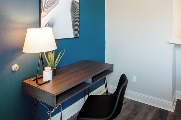 Un escritorio con una lámpara, una planta pequeña y una silla negra en una habitación con paredes azules y blancas.