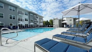 A swimming pool with lounge chairs and umbrellas, surrounded by multi-story buildings with balconies. - North Concord Apartments By Landing (Concord)