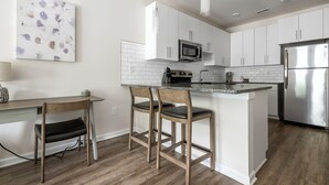 A modern kitchen with white cabinets, stainless steel appliances, and a wooden island with bar stools. - North Concord Apartments By Landing (Concord)