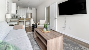 A modern living room with a grey sofa, a wooden coffee table, and a TV mounted on the wall. - North Concord Apartments By Landing (Concord)