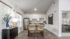 A modern kitchen with white cabinets, a dining table with wicker chairs, and a refrigerator. - North Concord Apartments By Landing (Concord)