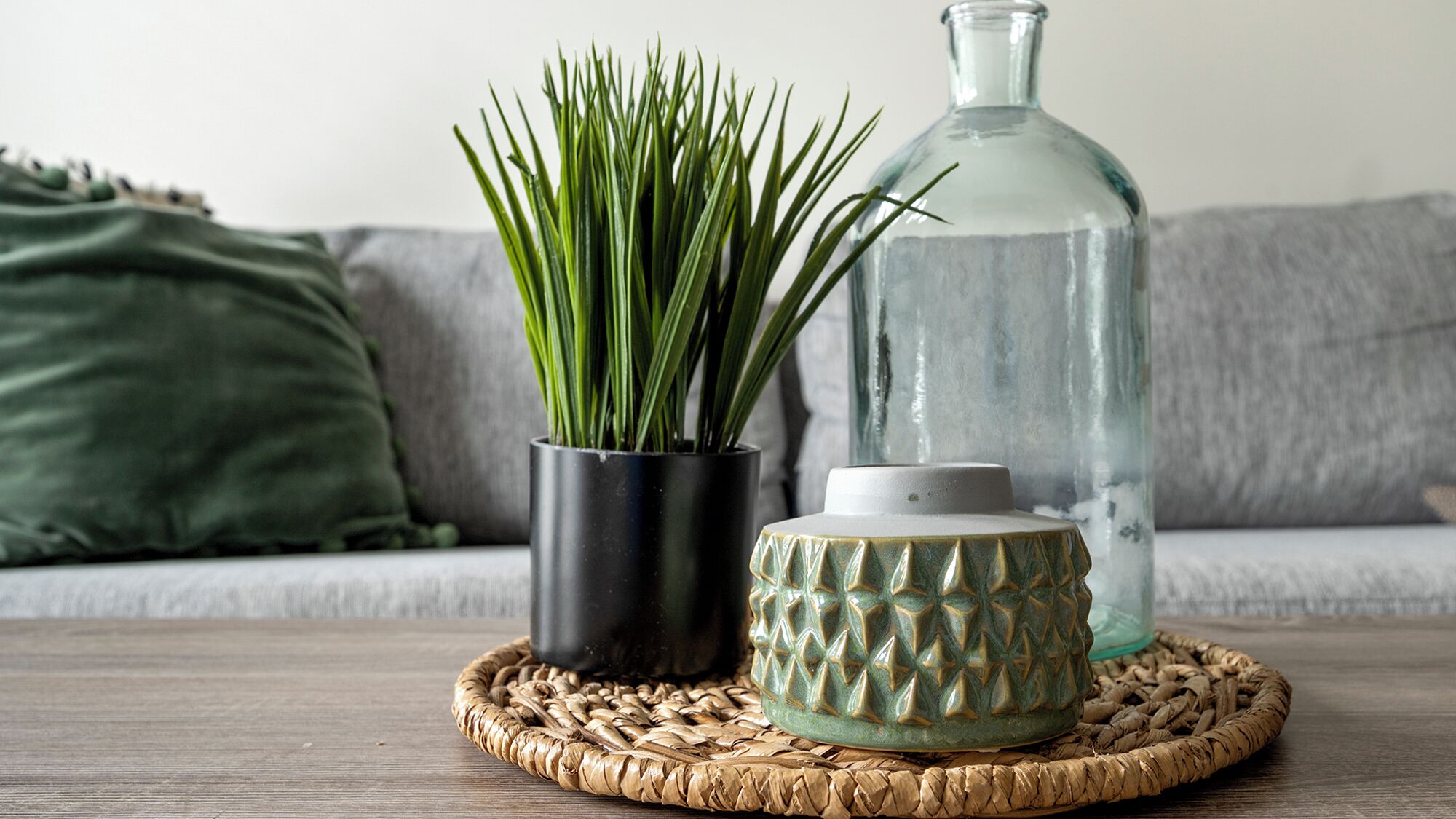 A woven placemat on a wooden table with a potted plant, a glass bottle, and a ceramic container.