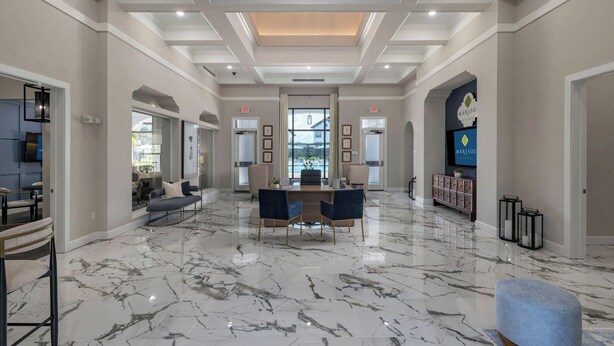 Um hall amplo com piso de mármore, balcão de recepção, assentos confortáveis e uma grande tela de televisão.