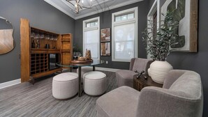 Uma sala de estar moderna com uma mesa de centro de vidro, cadeiras estofadas em cinza, um suporte de madeira para vinhos e uma grande planta em vaso.