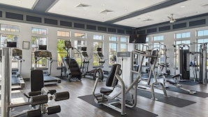 Uma academia com diversos equipamentos de exercícios, grandes janelas e piso de madeira.