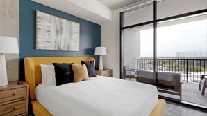 A modern hotel room with a large bed, a nightstand, a lamp, a view of the city through large windows, and a balcony with chairs. - Landing St. Petersburg Near South Branch Potomac River (St. Petersburg)