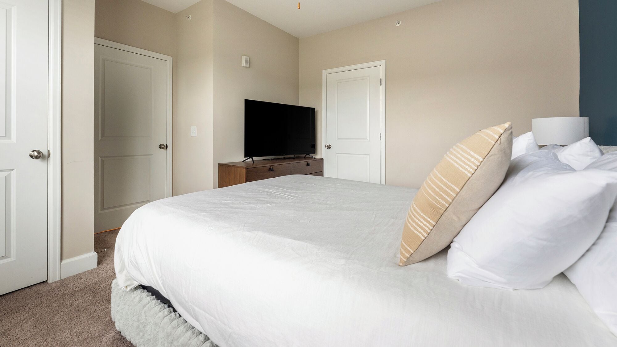 Un dormitorio con una cama, un televisor sobre un aparador de madera y dos puertas.