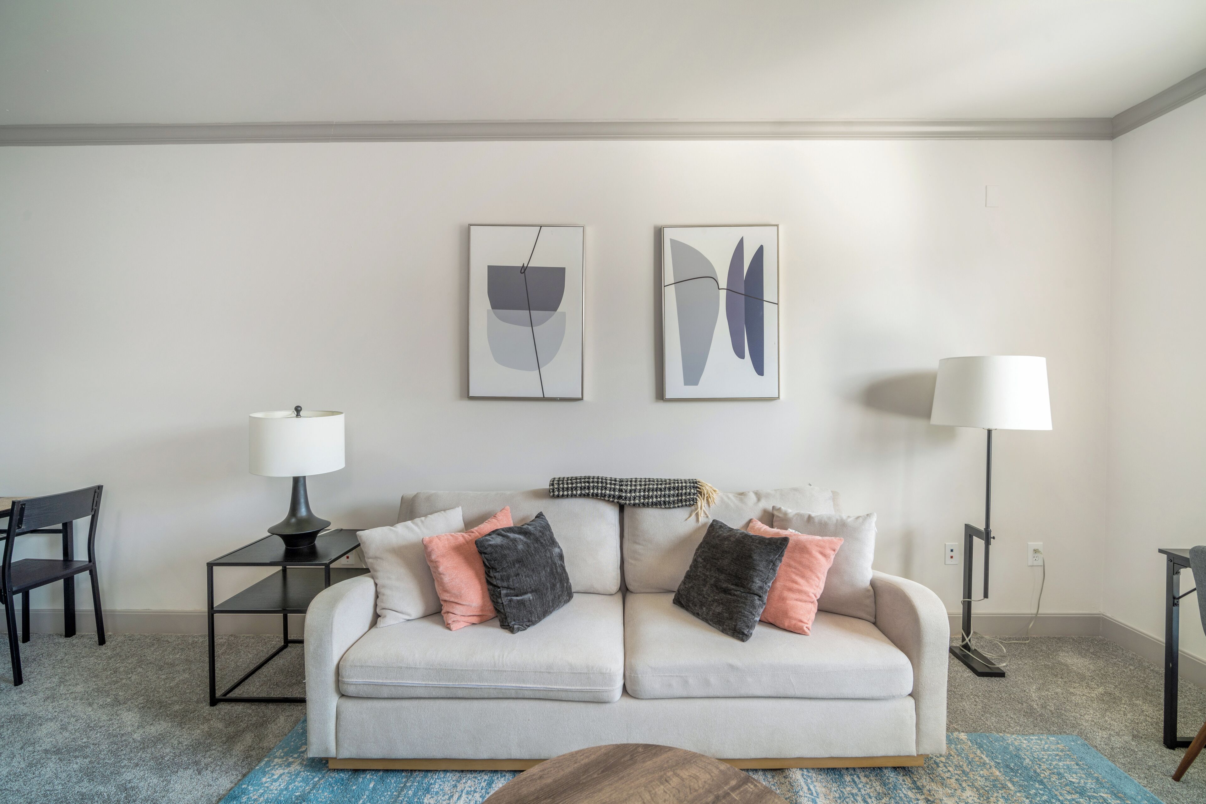 A living room with a sofa, two side tables, a lamp, and abstract wall art.