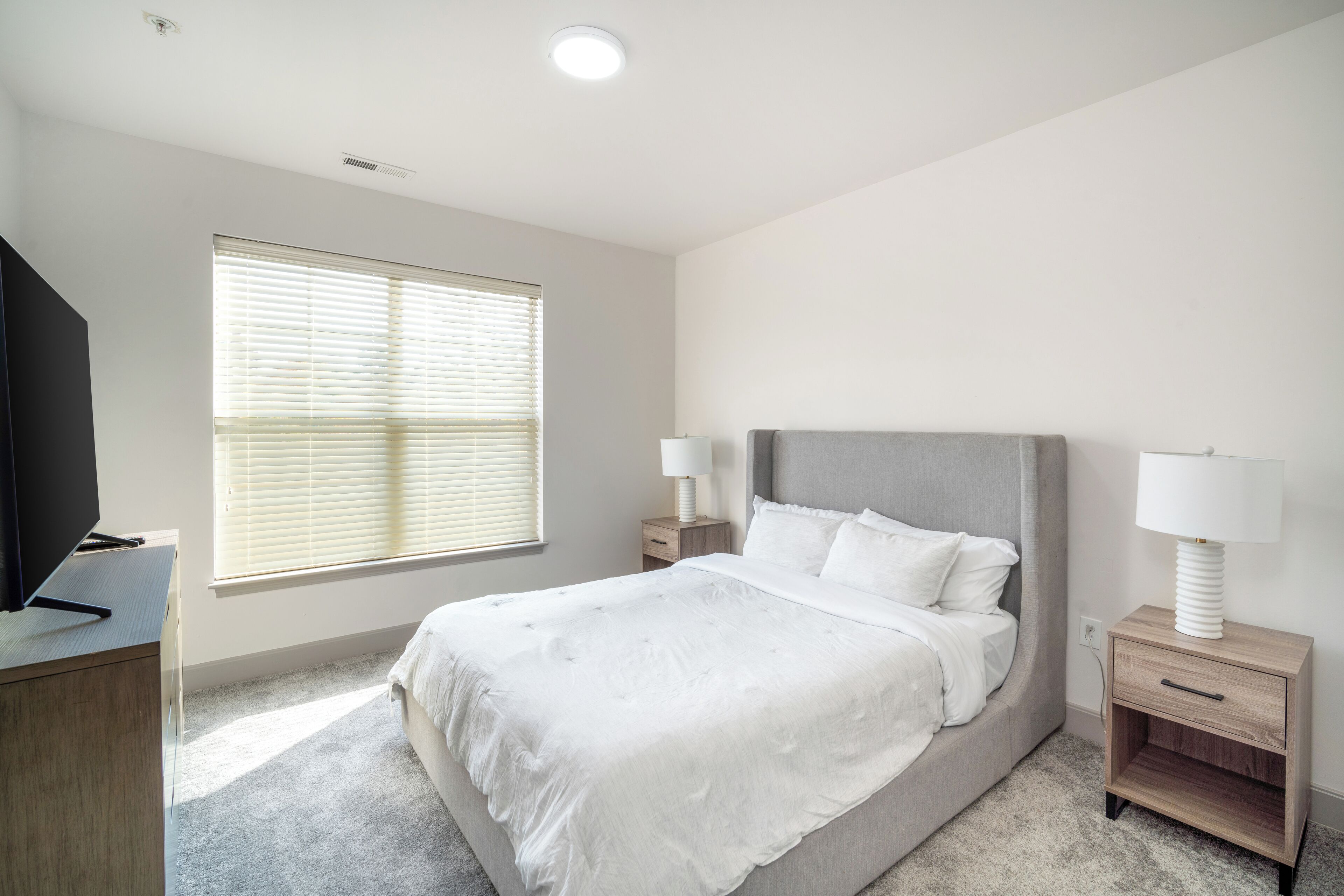 Un dormitorio con cama, mesitas de noche, escritorio y ventana con persianas.