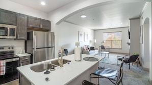 Een moderne keuken met roestvrijstalen apparatuur, een wit aanrecht en een eethoek met stoelen en een tafel.