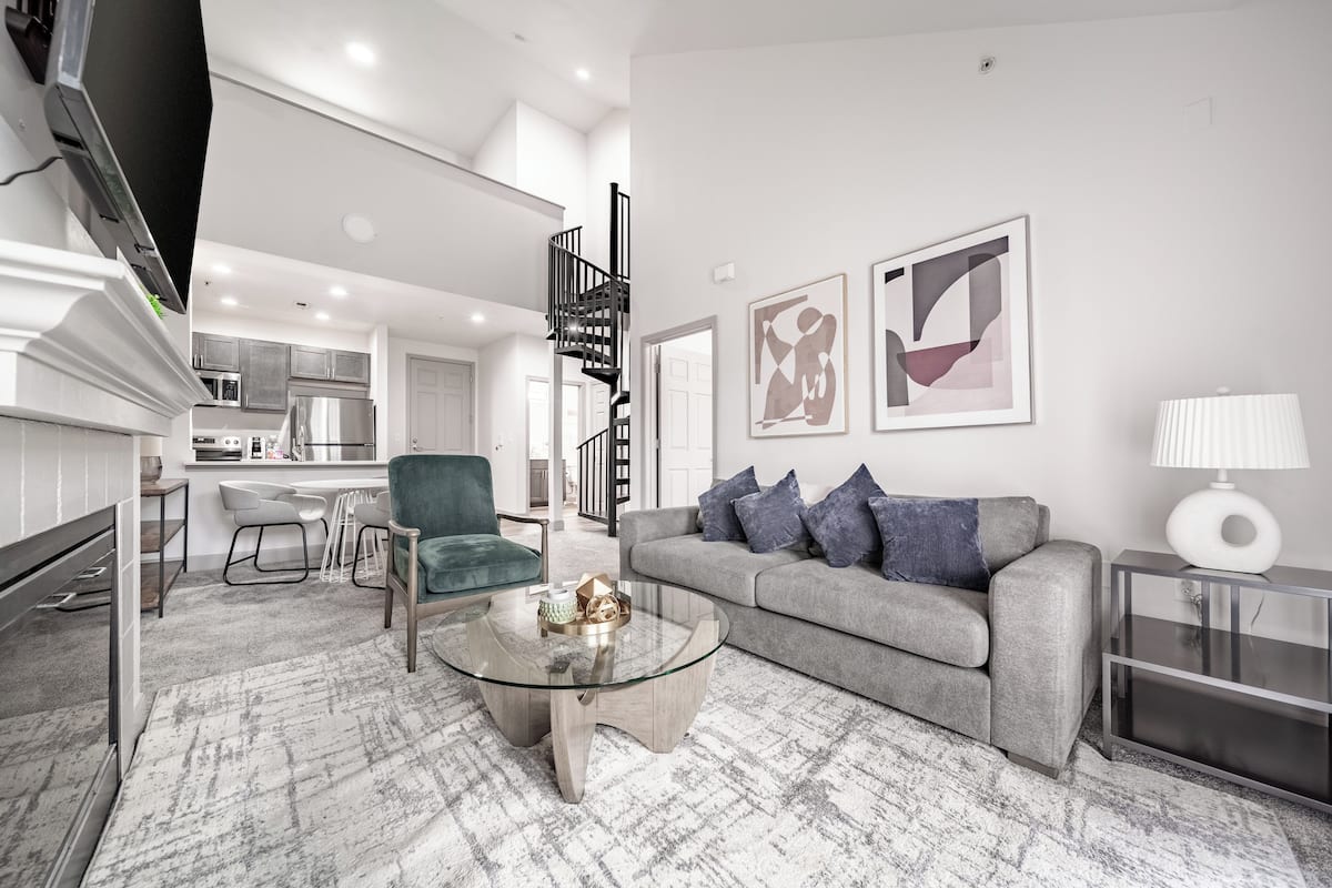 A modern living room with a grey sofa, a glass coffee table, and a spiral staircase leading to an upper floor.