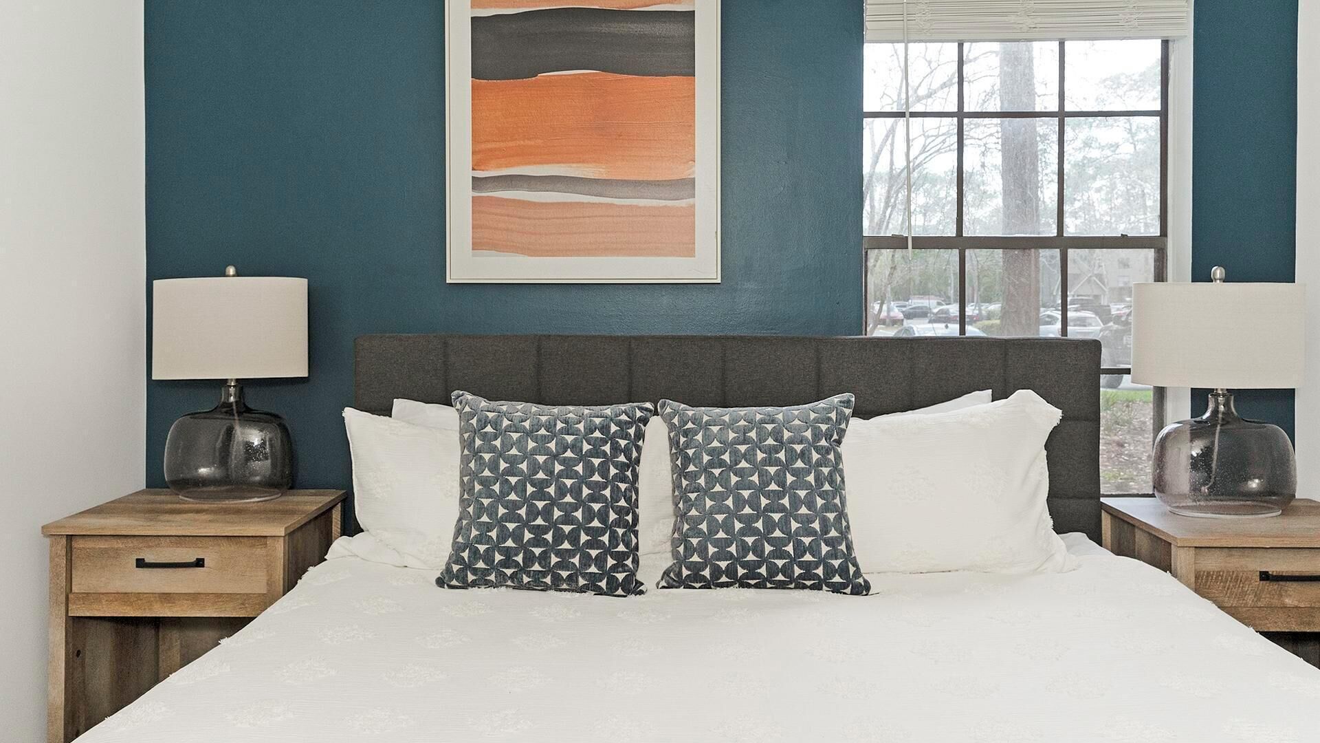 A bedroom with a bed, two nightstands, a window, and a wall art piece.