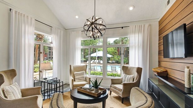 A modern living room with a round coffee table, two armchairs, and a sofa. Large windows offer a view of a pool and outdoor furniture. - Landing Jacksonville (Jacksonville)