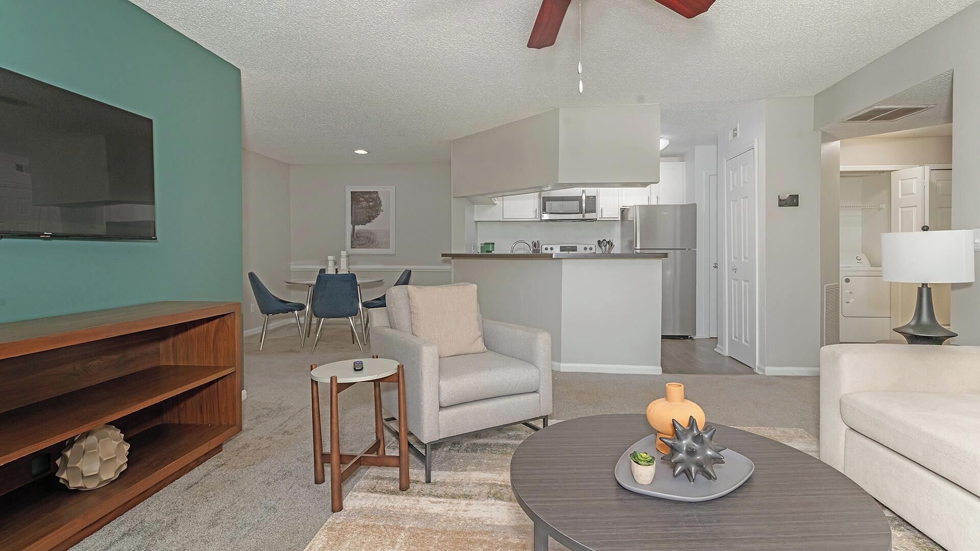 A modern living room with a TV, sofa, coffee table, and a kitchen in the background.