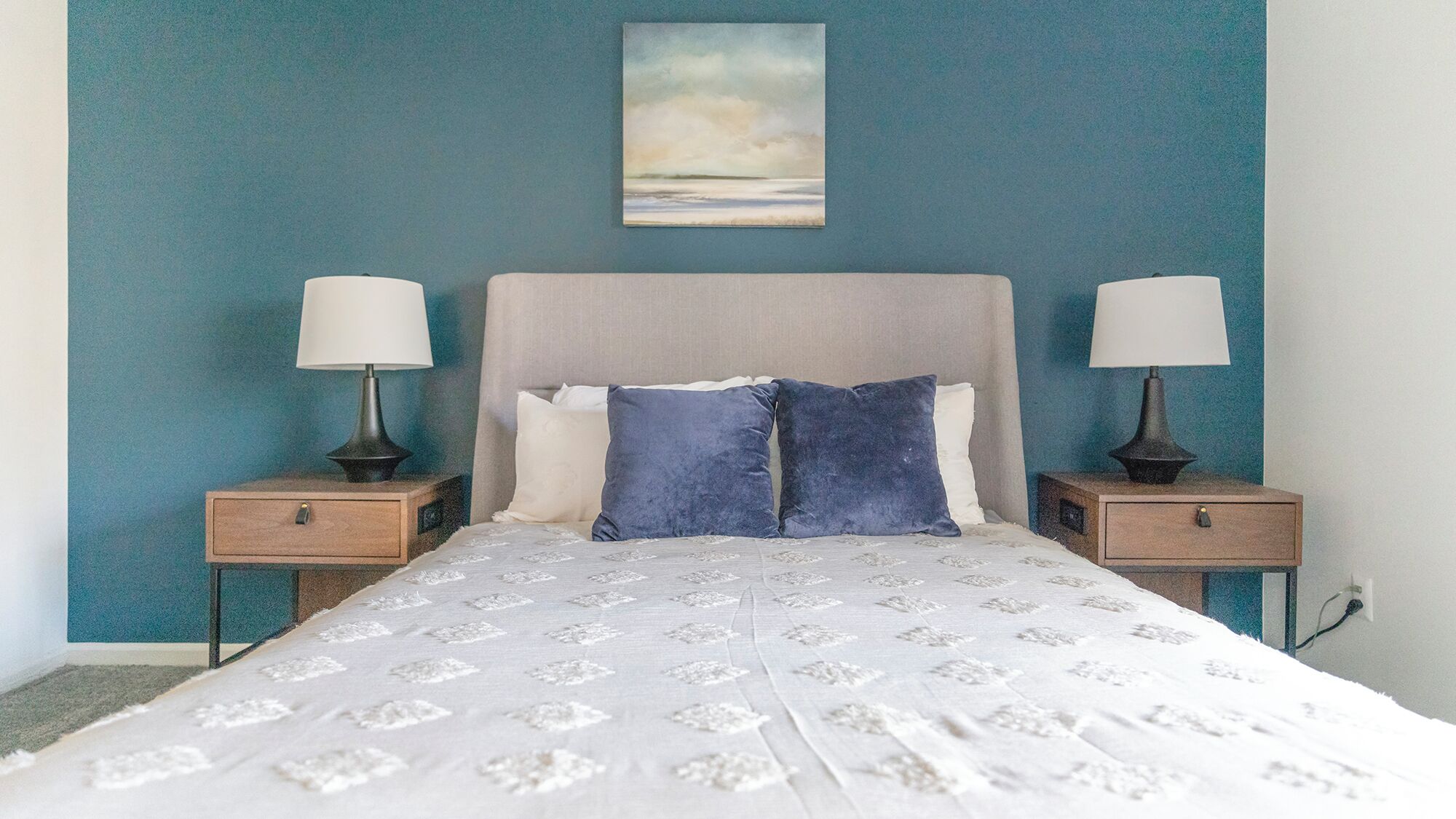 A bedroom with a bed, two bedside tables, and a painting on the wall.