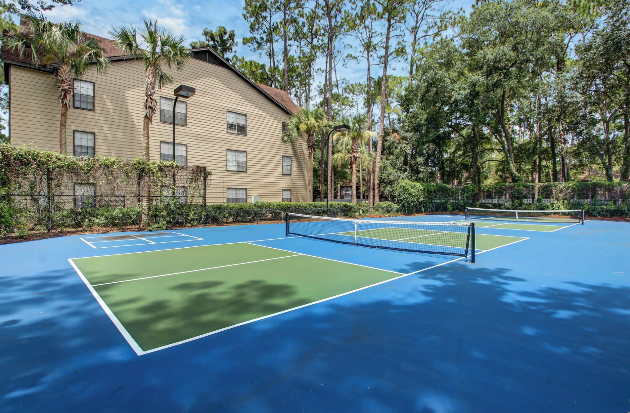 A tennis court with a net, surrounded by trees and a building with windows.
