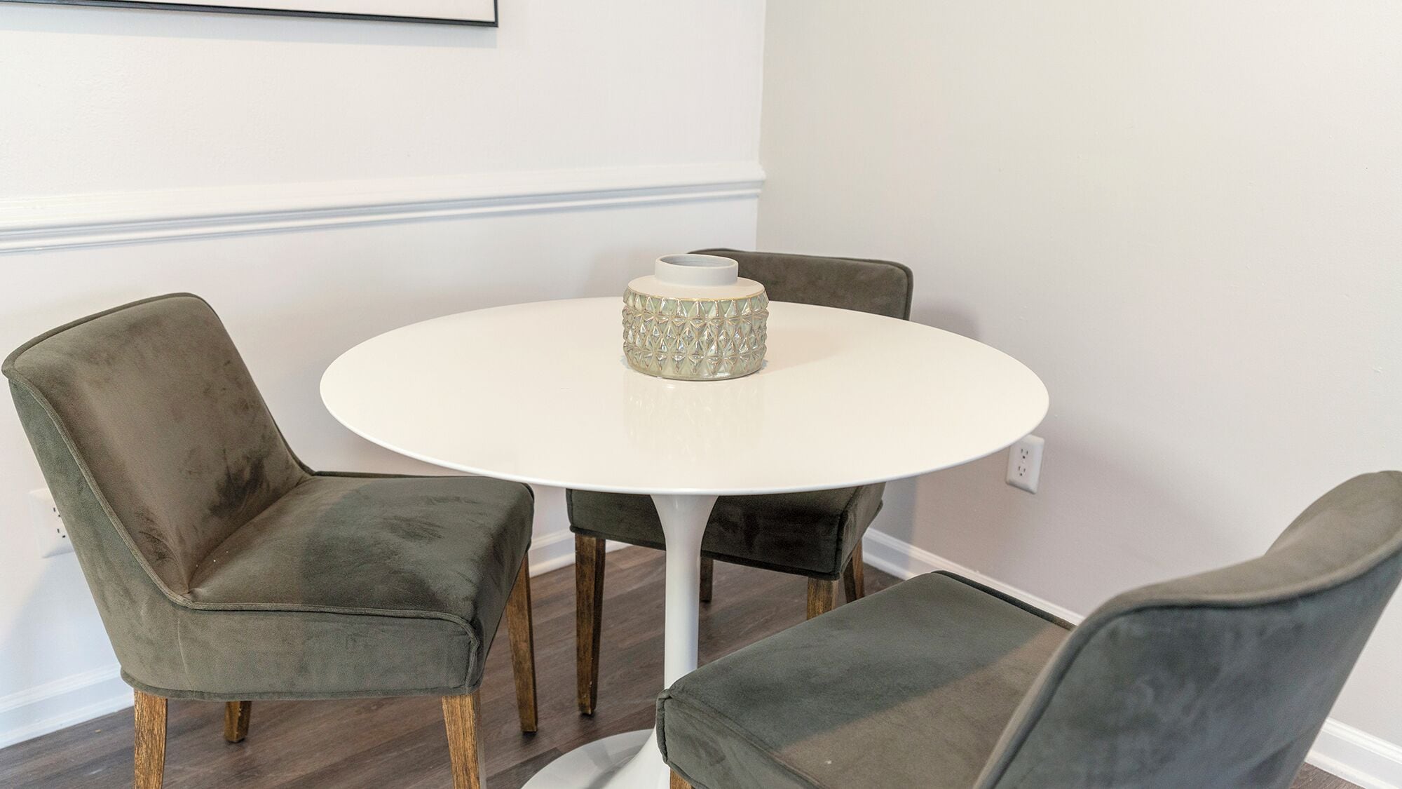 A round white table with a textured vase in the center, flanked by two upholstered chairs with wooden legs.