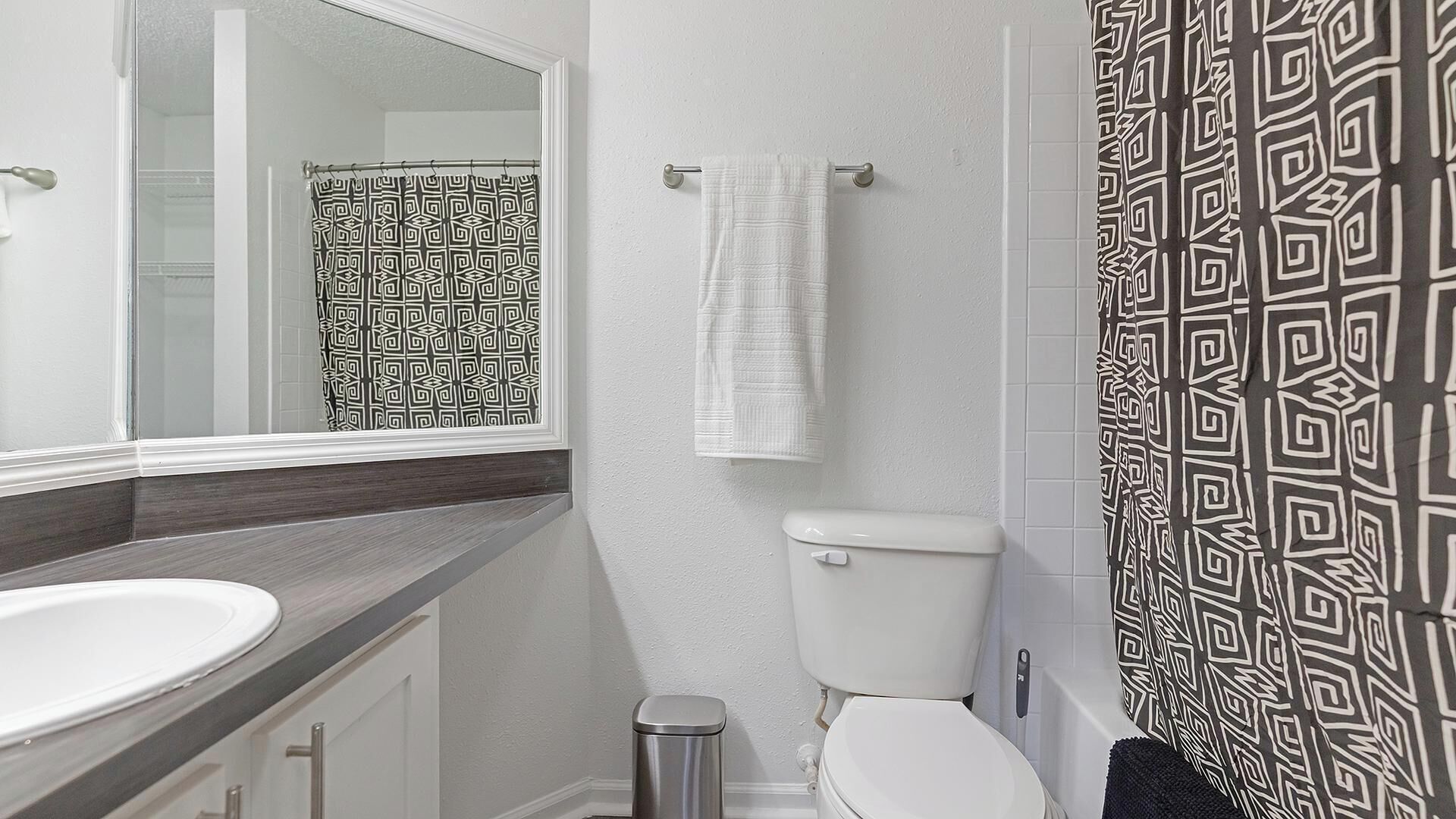 Ein Badezimmer mit einem weißen Waschbecken, einer Toilette und einer Duschkabine mit geometrischem Muster.