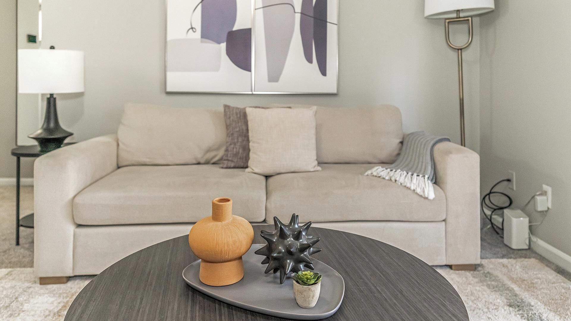 A living room with a beige sofa, a round coffee table with decorative items, and a modern lamp.