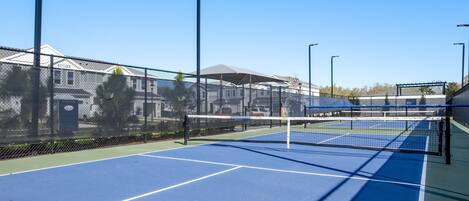An outdoor tennis court with a net, surrounded by a chain-link fence.