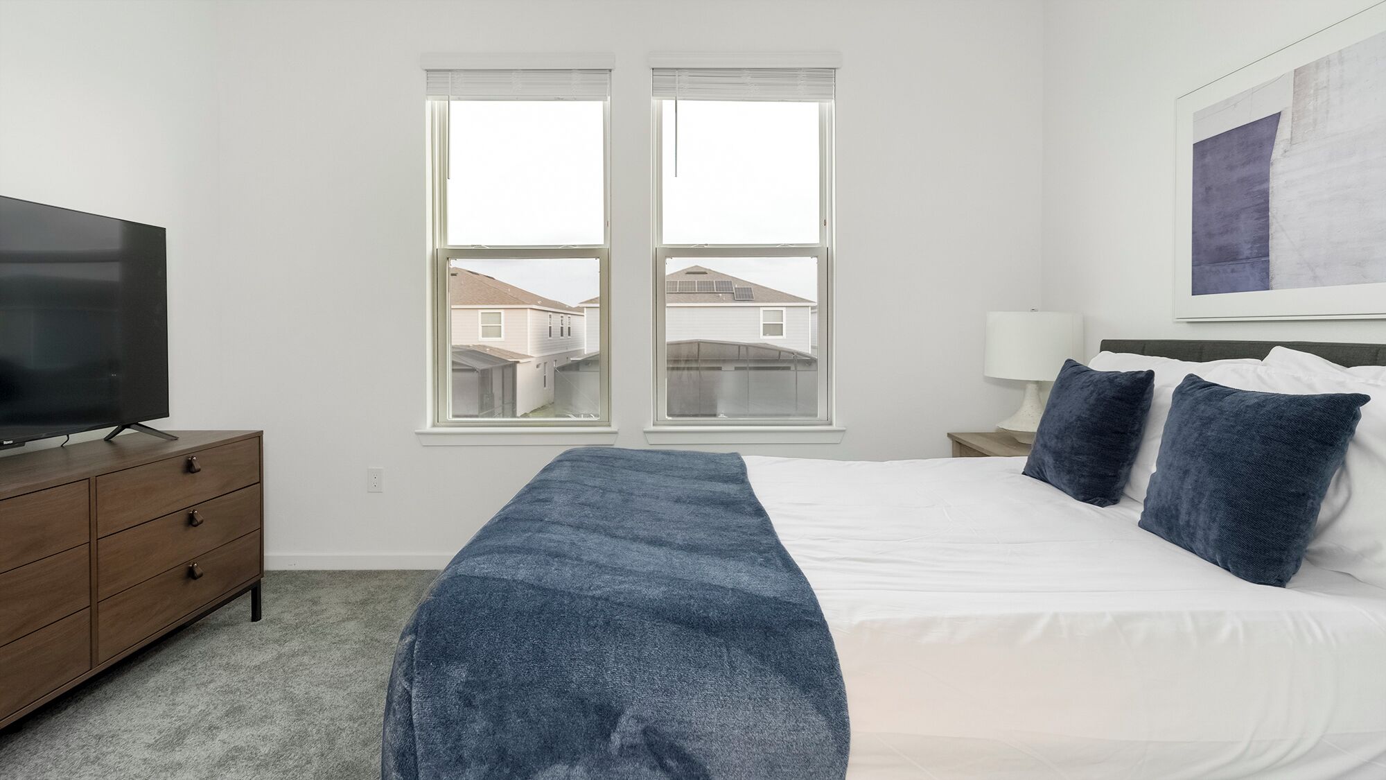 A bedroom with a bed, a TV on a dresser, a window, and a painting on the wall.
