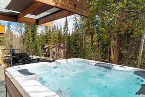 Een hottub omringd door bomen, een houten terras en tuinmeubilair.