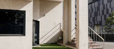 A building with a staircase, a window, and a small patch of grass.