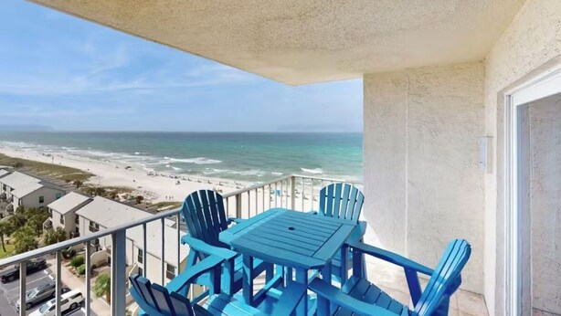 A balcony with a table and chairs, overlooking a beach and ocean.