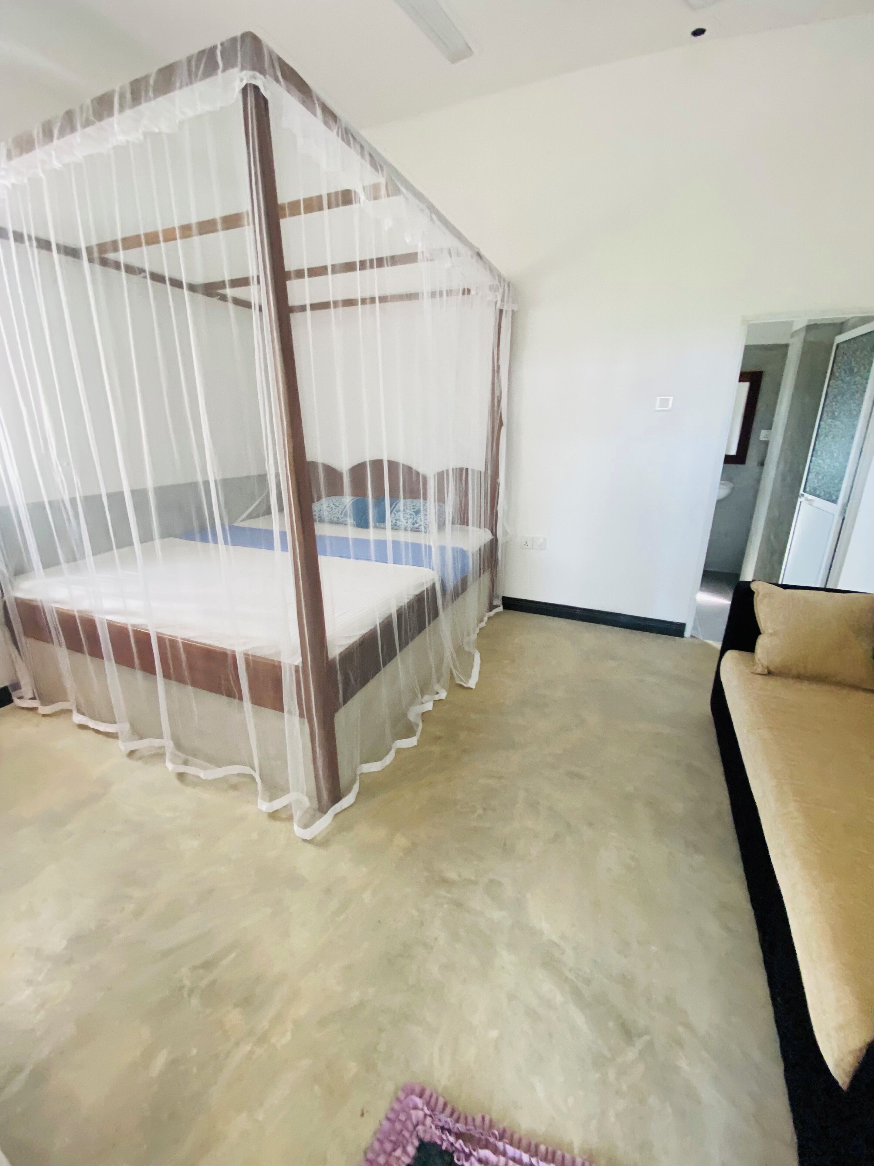 A room with a four-poster canopy bed, a beige sofa, and a small rug.
