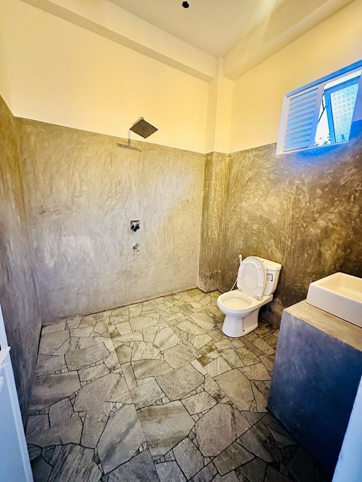 A bathroom with a stone floor, a toilet, and a sink.