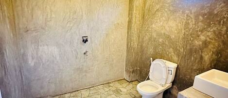 A bathroom with a stone floor, a toilet, and a sink.