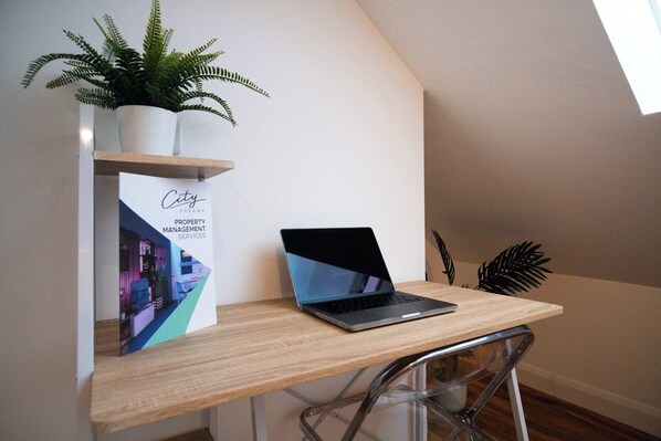 A laptop on a wooden desk with a potted plant and a brochure. - Chic Apartment w/ Fast London Access & WiFi (London)