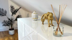 A white, reflective surface with a gold monkey figurine, a white vase with gold patterns, and reed diffusers. - Stylish Apartment in Buckhurst Hill (London)
